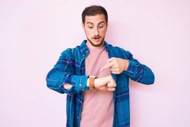 Gündelik giysiler giymiş genç yakışıklı adam, saati, sabırsızlığı, gecikme yüzünden kızgın ve sinirli olduğunu gösteriyor. 