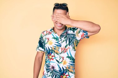 Yazlık giysiler giyen, gülümseyen ve gülen genç, yakışıklı latin adam şaşırtmak için gözlerini kapatıyor. kör kavram. 