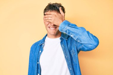 Gündelik kıyafetler giyen, gülümseyen ve gülümseyen genç yakışıklı adam şaşırmak için gözlerini kapatıyor. kör kavram. 