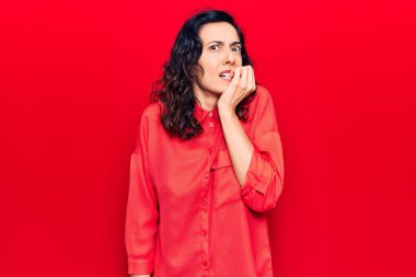 Gündelik kıyafetler giyen genç, İspanyol bir kadın gergin ve gergin görünüyor. Ağzı tırnak yiyen ellerle. anksiyete. 