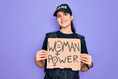 Güvenlik kurşungeçirmez yelek giyen kadın polis memuru elinde gülen bir yüzle ayakta duran ve gülümseyen dişlerini gösteren kadın güç gösterisi kartonuyla protesto ediyor.