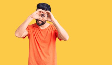 Sakallı, sıradan tişörtlü, kalp şeklinde el ve parmakları olan genç ve yakışıklı bir adam tabeladan bakıp gülümsüyor. 