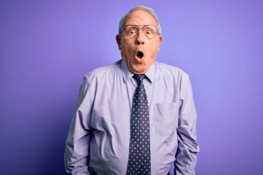Gri saçlı, gözlüklü, gözlüklü, mor tenli bir iş adamı. Korkmuş ve şok olmuş bir halde..