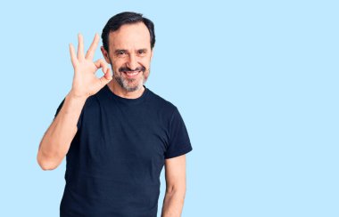 Orta yaşlı yakışıklı bir adam günlük tişört giyiyor, gülümsüyor ve el ve parmaklarıyla 