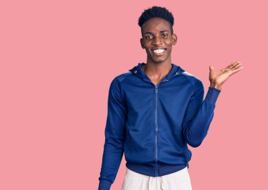 Afro-Amerikalı genç adam spor giysisi giyiyor. Gülümsüyor, gülümsüyor ve avuç içi kadar kameraya bakıyor.. 