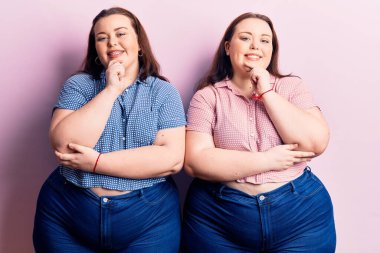 Genç ve cüsseli ikizler gündelik kıyafetler giyip kameraya bakıyor kollarını kavuşturup gülümsüyor ve ellerini çenesine kaldırıyor. Olumlu düşünmek. 