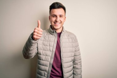 Kışlık ceket giyen yakışıklı beyaz bir adam izole bir arka planda duruyor ve elleriyle mutlu bir jest yapıyor. Kameraya bakıp başarıyı gösteren ifade onaylanıyor.