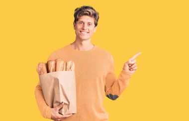 Elinde ekmek torbası olan genç yakışıklı adam gülümsüyor mutlu bir şekilde elini ve parmağını yana uzatıyordu. 