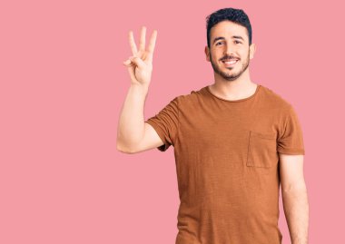 Gündelik kıyafetler giyen genç İspanyol adam üç numarayı gösterip işaret ederken kendinden emin ve mutlu gülümsüyor.. 