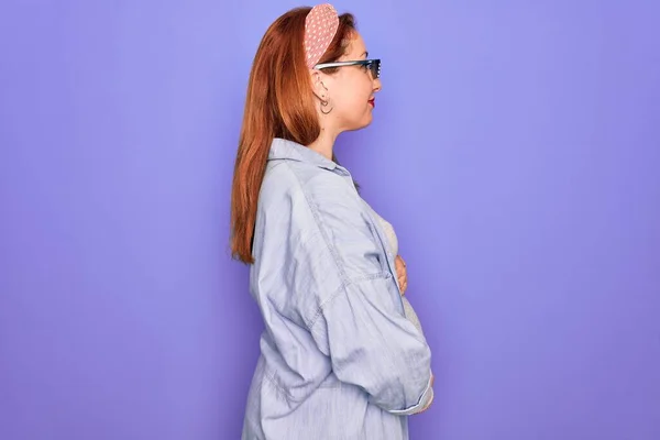 Young redhead pregnant woman expecting baby wearing funny thug life sunglasses looking to side, relax profile pose with natural face with confident smile.