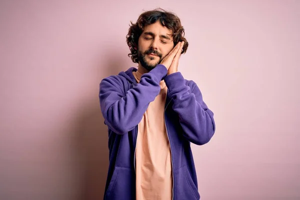 Young handsome sporty man with beard wearing casual sweatshirt over pink background sleeping tired dreaming and posing with hands together while smiling with closed eyes.