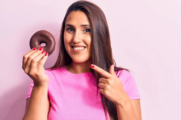 Joven Hermosa Morena Sosteniendo Donut Chocolate Sonriendo Feliz Señalando Con — Foto de Stock