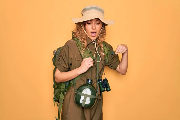 Young blonde explorer woman with blue eyes hiking wearing backpack and water canteen Pointing down with fingers showing advertisement, surprised face and open mouth