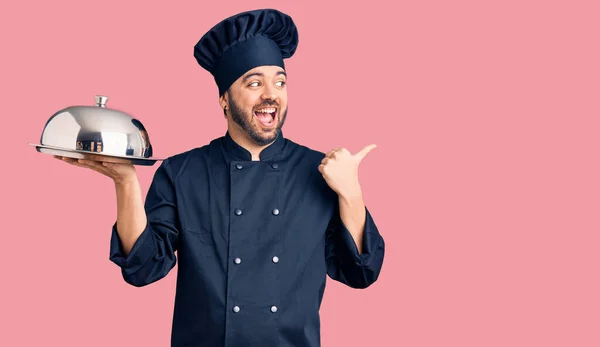 Joven Hispano Con Uniforme Cocina Sosteniendo Bandeja Apuntando Con Pulgar —  Fotos de Stock