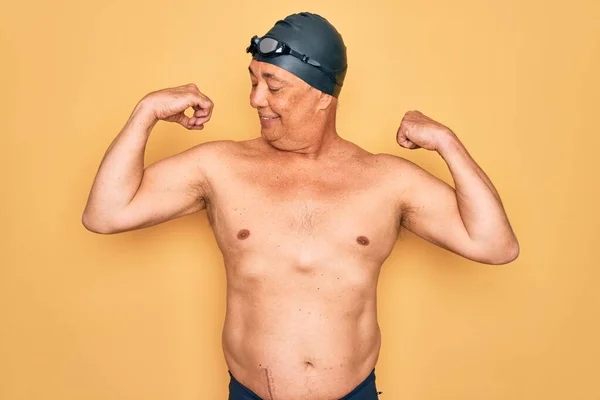 中年白发男子 身穿泳衣 头罩和护目镜 露出手臂肌肉 洋洋得意地笑着 健康概念 — 图库照片