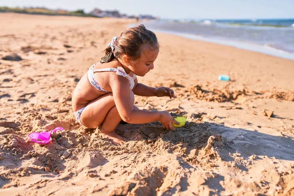ビキニを着た愛らしいブロンドの子供 ビーチでバケツやシャベルを使用して砂の城を構築する — ストック写真