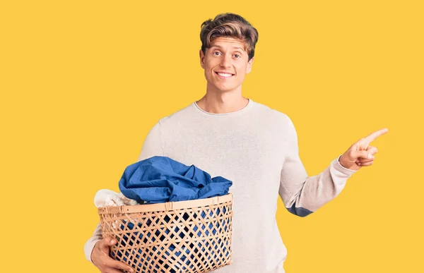 Joven Hombre Guapo Sosteniendo Cesta Ropa Sonriendo Feliz Señalando Con — Foto de Stock