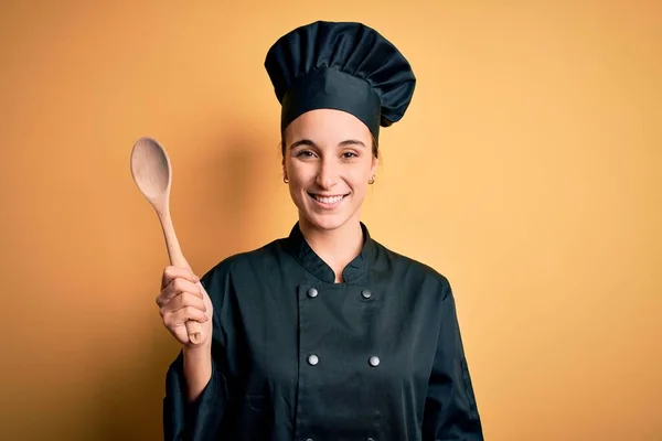 年轻美丽的厨师女士 身穿炊事服 头戴帽子 手持木勺 笑容满面 露出自信的笑容 露出牙齿 — 图库照片