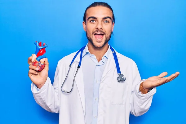 Jovem Homem Bonito Vestindo Estetoscópio Médico Segurando Coração Celebrando Realização — Fotografia de Stock