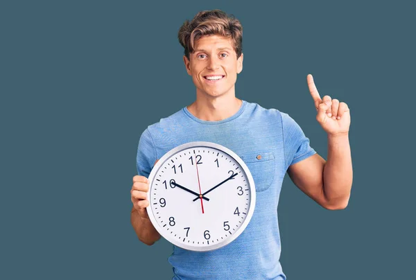 Joven Hombre Guapo Sosteniendo Gran Reloj Sorprendido Con Una Idea —  Fotos de Stock