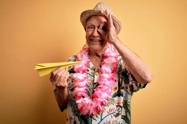 グレー毛シニア男身に着けています夏の帽子とHawaiianレイ保持紙飛行機休暇で幸せな顔笑顔します — ストック写真