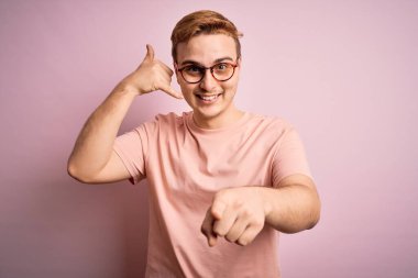 Genç, kızıl saçlı, sıradan bir tişört giyen, pembe arka planda duran, gülümseyen, telefonda konuşan ve seni işaret eden genç bir adam. Ara beni..