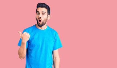 Sıradan tişörtler giyen sakallı genç yakışıklı bir adam elleri yana dönük, ağzı açık şaşkın bir ifadeyle şaşırdı.. 