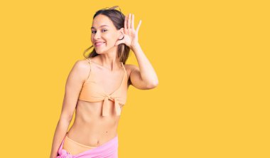 Bikini ve güneş gözlüğü takan güzel esmer bir kadın. Kulağından kulağa gülümsüyor. Dedikoduları ve dedikoduları dinliyor. Sağırlık kavramı. 