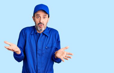 Orta yaşlı, yakışıklı, mekanik üniforma giyen, kolları açık ve kafası karışık bir adam. Konseptten bihaber.. 