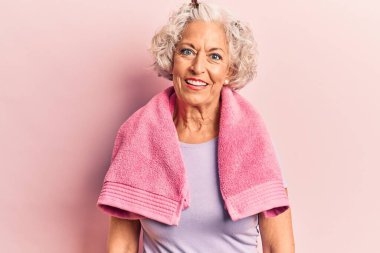 Kıdemli gri saçlı kadın spor giysi ve havlu giyiyor ve yüzünde mutlu ve havalı bir gülümseme var. şanslı kişi. 