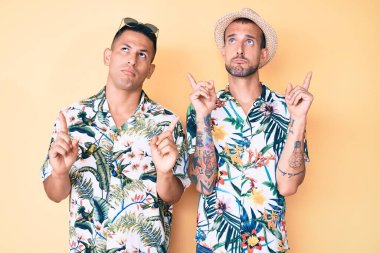 Yazlık şapkalı ve Hawaii tişörtlü iki genç gay üzgün ve üzgün görünüyor, parmaklarıyla yönü gösteriyor, mutsuz ve depresif.. 