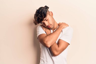 Gündelik kıyafetler giyen genç İspanyol adam kendine sarılıyor mutlu ve pozitif, kendinden emin gülümsüyor. Sevgi ve özgüven. 