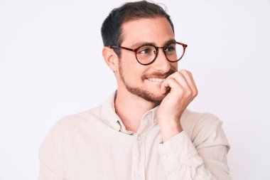 Gündelik kıyafetler ve gözlük takan genç yakışıklı adam gergin ve gergin görünüyor. Elleri ağızdan tırnak yiyor. anksiyete. 