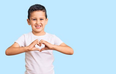 Sevimli çocuk, günlük beyaz tişörtler giyiyor. Sevgiyle gülümsüyor. Elleriyle kalp sembolü ve şekli gösteriyor. romantik kavram. 