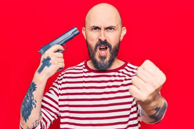 Genç, yakışıklı bir adam silah tutuyor sinirlenmiş ve sinirlenmiş öfkeyle bağırıyor, öfkeyle bağırıyor ve el kaldırıyor. 