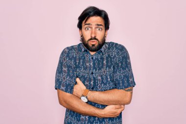Yakışıklı İspanyol bohem bir adam pembe arka planda hippi tarzı giyinmiş soğuk kış soğuğu için titriyor ve donuyor yüzünde üzgün ve şok ifadesi var.