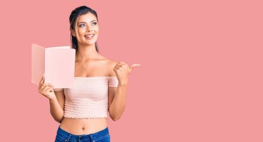 Genç, güzel bir kadın, elinde kitapla baş parmağını kaldırmış, ağzı açık gülümsüyor. 