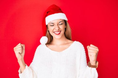 Genç esmer kadın Noel şapkası takıyor. Çok mutlu ve heyecanlı. Kazanan bir jest yapıyor. kutlama konsepti. 