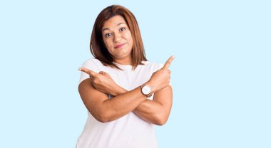 Orta yaşlı, beyaz tişört giyen, her iki tarafı da parmaklarıyla gösteren Latin kadın farklı yönlere bakıyor. 