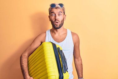 Tatilde, güneş gözlüğü takan genç, sarışın bir turist uçak kamarası çantası tutuyor.