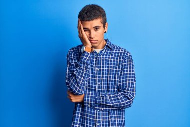 Genç Afro-Amerikalı bir adam günlük kıyafetler giyip kollarını kavuşturarak depresyondan sıkılmış ve yorgun görünüyor.. 