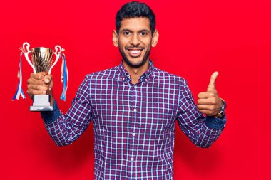 Genç latin adam elinde kupa tutuyor mutlu ve pozitif gülümsüyor, başparmağıyla mükemmel ve onay işareti yapıyor. 