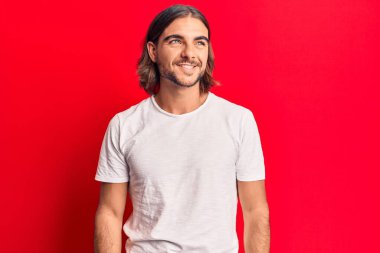 Gündelik giysiler giymiş genç yakışıklı bir adam yüzünde gülümsemeyle yan yana bakıyor, doğal bir ifade. Kendinden emin gülen. 