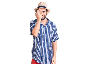 Sakallı, yaz şapkalı ve çizgili gömlekli genç yakışıklı bir adam bir gözünü eliyle kapatıyor, yüzünde kendine güvenen bir gülümseme ve sürpriz bir duygu var.. 