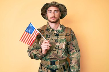 Kafkasyalı genç adam kamuflaj üniforması giyiyor. Amerikan bayrağını taşıyor. Düşünme ve ayık görünme. 