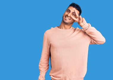 Gündelik kıyafetler giyen genç İspanyol adam barış sembolü yapıyor. Yüzünde parmaklar, gülümseyerek zaferi gösteriyor. 