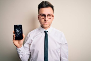 Akıllı telefonu olan yakışıklı beyaz bir adam izole edilmiş arka planda kırık bir ekran tutuyor. Akıllı yüzünde kendine güvenen bir ifade var ve ciddi düşünüyor.