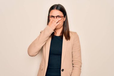 Beyaz arka planda ceket ve gözlük takan genç, güzel esmer iş kadını pis ve iğrenç bir koku alıyor, nefesini burnunda tutuyor. Kötü kokuyor.