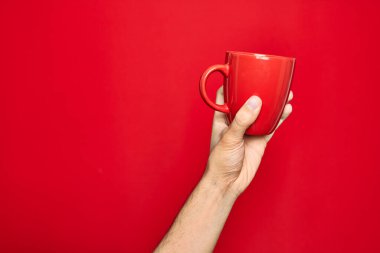 İzole edilmiş kırmızı arka planda bir fincan kahveyi tutan adamın güzel eli