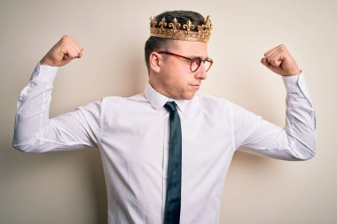 İzole edilmiş arka planda altın taç takan yakışıklı beyaz iş adamı gururla gülümseyen kol kaslarını gösteriyor. Fitness konsepti.